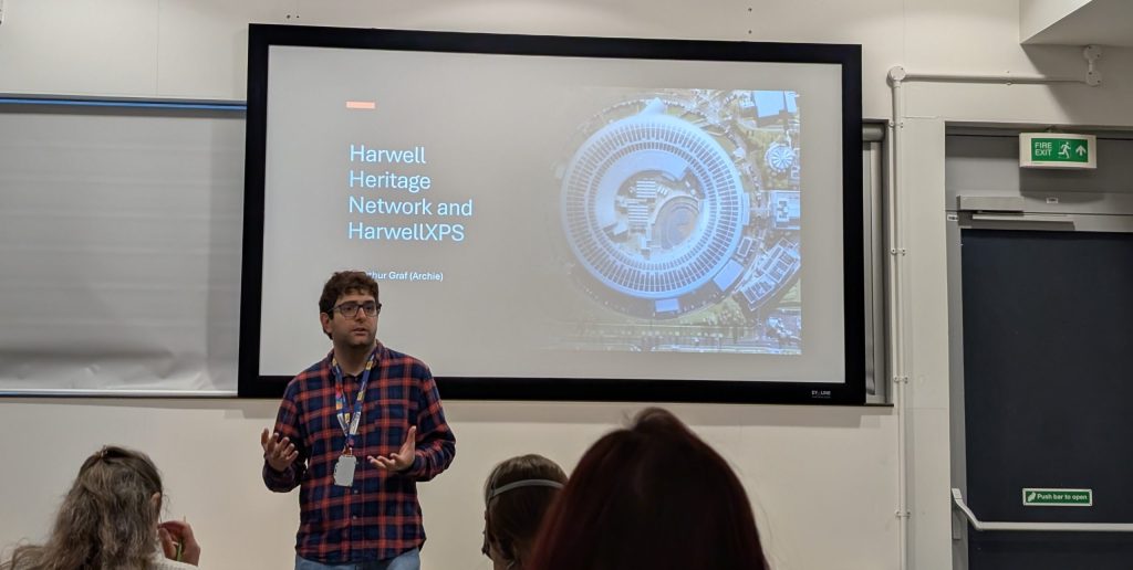 Dr. Archie Graf presenting to an audience the opening message in front of a screen with title slide named 'Harwell Heritage Network and HarwellXPS'.