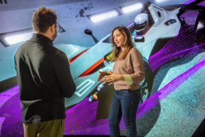 Two people talking in front of a automotive graphic 